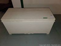 Top-down front view of white wooden chest on concrete floor, showing some surface scratches and wear.