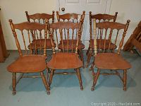 Front view of six solid maple dining room chairs with turned legs and decorative spindle backs.