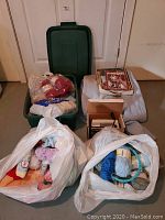Full view of the lot showing yarn in plastic bags, fabric, iron, Rubbermaid container, and knitting design books.