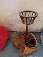 Solid oak plant stand made of wood with spindle design and circular top, shown next to several wicker baskets including horn of plenty and heart-shaped basket