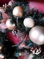 Close-up of part of the Kirkland Holiday prelit wreath showing gold and cream baubles, pinecones, decorative leaves, and integrated string lights