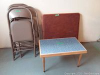 Photo shows four metal folding chairs stacked beside a blue marbled laminate card table and a square wooden panel likely the underside or top of the card table.