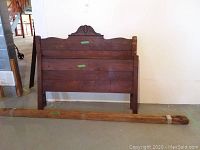 Photo of the full wooden headboard and footboard leaning against a wall with the wooden frame slats on the floor in front.