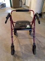 Front view of red walker showing padded seat, brakes on handles, and four wheels