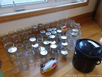 Glass canning jars arranged on floor in multiple rows with metal lids and a small canning pot to the right.