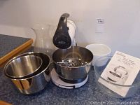 Full view of Sunbeam Mixmaster stand mixer with set of mixing bowls and clear glass vase on countertop.