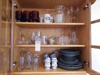 Glassware items including wine and champagne glasses on shelves along with blue-grey ceramic mugs, dark blue plates and bowls, and clear beverage jug.