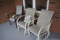 Photo showing three outdoor deck chairs on a porch, two cream metal mesh rocking chairs with floral cushions and one black metal chair with beige cushion.