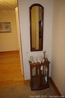 View of the wood display cabinet with glass doors and some small décor items on top, adjacent to the wood framed wall mirror hung on a wall.