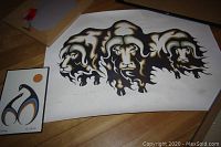 Two Indigenous art prints on a wooden surface: one small framed print titled 'Comforting' by Doris Cyrette, and one larger unframed triple-headed animal print by Guy Aerts.
