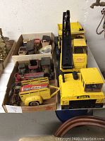 View of large yellow Tonka Mighty Tonka crane truck and multiple boxes of assorted vintage toy cars including a yellow Mobil trailer