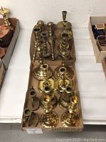 Top view of two trays with eight sets of brass candle holders showing variety of styles and base shapes