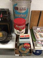 Photo showing large blue Sweetex shortening tin, Campbell's Tomato Soup tin, and assorted smaller tins and boxes in a cardboard box.