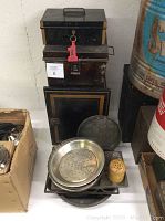 Photo showing stacked vintage metal baker's boxes with gold trim and some miscellaneous bakeware laid in front including pie pans and a yellow dough docker.
