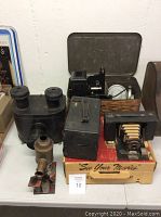 Black folding bellows camera, box camera with handle, and brass lens/viewer on a table