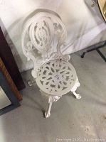 Front and side view of white cast-iron decorative garden chair showing ornate backrest and round seat with cut-out pattern.