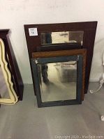Photo of four assorted vintage mirrors stacked against a wall, showing various wooden frame styles and sizes.