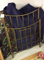Metal bed frame headboard and footboard leaning against padded furniture covers, showing classic vertical and horizontal bar design with brass or bronze finish.
