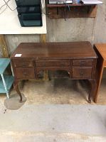 Front view of the wooden desk showing the five drawers and veneer wear on top and sides.