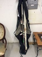 Fischer skis and ski tote bag shown upright leaning against a wall with ski poles inside the tote bag.