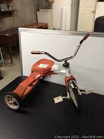 Side and angle view of Roadmaster tricycle showing orange seat, white frame, and chrome handlebars.