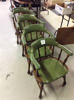 Four green vinyl captain chairs with wooden frames arranged in a row in a warehouse setting