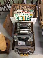 Photo showing 4 vintage car radios stacked below a box holding license plates, including a Florida plate in front.