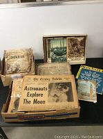 Full view of boxes containing newspapers and brochures including the moon landing headline newspaper and French travel brochures