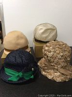 Photo showing four women's hats on boxes and surface, variety of styles and materials visible