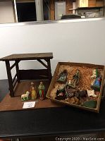 Full view of wooden stable next to box containing multiple manger figures including human and animal figures.