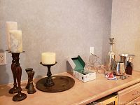 Two pairs of candlestick holders including tall pillar holders with candles and smaller hexagonal distressed holders, a distressed copper colored platter, and various wine accessories including wine bottle rack, decanter, bottle chillers, corkscrew and bottle stoppers on a countertop.