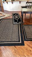 Three rugs on hardwood floor: large black speckled rectangular rug, smaller matching one, and black ornate runner.