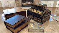 Six decorative storage boxes arranged on floor near fireplace, varying in wood, cardboard, and glass materials with floral and faux leather textures.