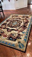 Angle view of entire rectangular area rug on hardwood floor showing ornate black and blue medallion design.