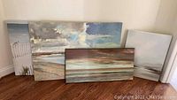 Group of four beach scene canvases leaning against wall