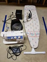 Full lot photo showing sewing machine, foot pedal, fan, heater, iron on ironing board.