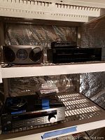 Wide-angle view of shelving with Emerson CD player, Sanyo cassette deck, Radio Shack speaker center, Sony stereo receiver, and stack of CDs.