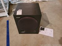 Full view of Sony SA-WM250 subwoofer with instruction manual placed beside it on ground.