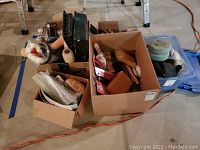 Overall photo of all boxes of paint and polishing supplies on floor including brushes, rollers, trays, sponges, power tools and accessories.