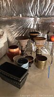 Photo shows assortment of planter pots and pedestals with large ceramic pot and wicker trashcan in basement setting