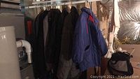 Photo of blue and olive green coats hanging on metal rack in a basement storage area with visible infrastructure
