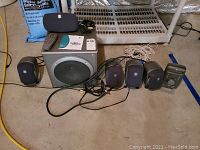 Full view of the Logitech Z-680 speaker system components including subwoofer, satellite speakers, touch control center, remote, and cables arranged on floor.