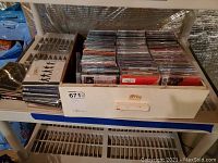 Wooden drawer filled with rows of CD jewel cases, stacked and organized together showing a large collection of CDs.