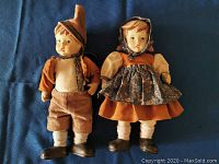 Front view of the boy and girl jointed German dolls standing side by side wearing traditional clothes on a blue background.