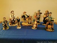 Photo showing the full set of eight men figurines arranged on a blue cloth, showing various poses and sizes.