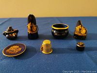 Full view of the miniature collection arranged on blue cloth showing piano, stool, pitcher, chamber pot, sugar bowl, plate, and thimble for scale
