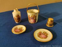 Four Limoges miniature porcelain items arranged on blue fabric, showing vase, bucket, two plates, and size reference thimble