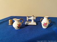 Photo showing three miniatures: a porcelain sewing machine, two pitchers, and a thimble for scale reference.