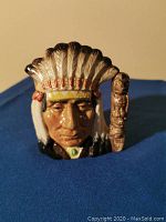 Front view of Royal Doulton character jug featuring a Native American man in feathered headdress with detailed facial features and small totem staff handle.