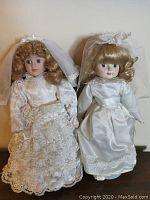Front view of two bride dolls in white bridal gowns and veils, positioned side by side.